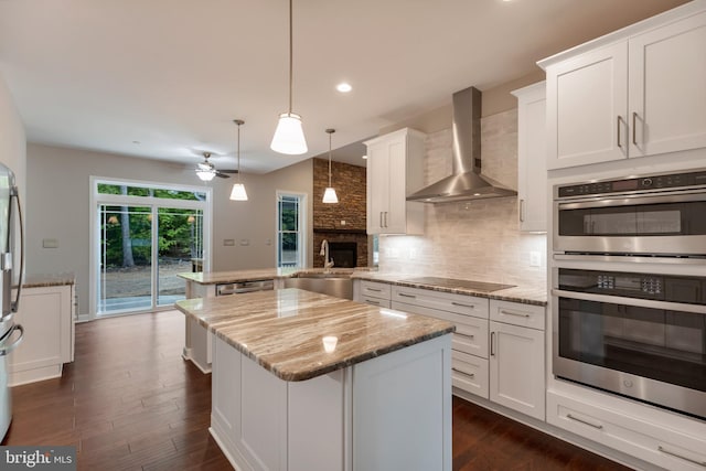 kitchen with sink, wall chimney range hood, kitchen peninsula, white cabinets, and appliances with stainless steel finishes