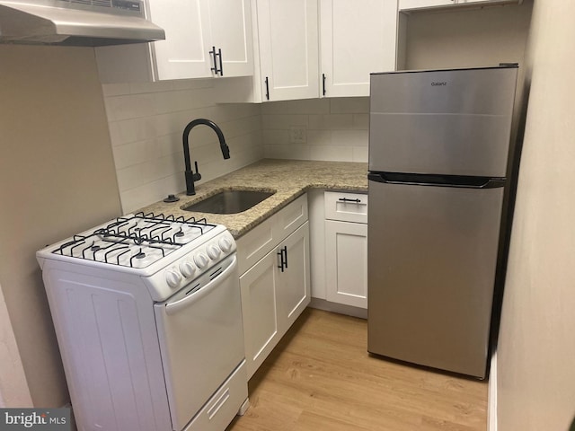 kitchen featuring light stone countertops, stainless steel fridge, gas range gas stove, extractor fan, and sink