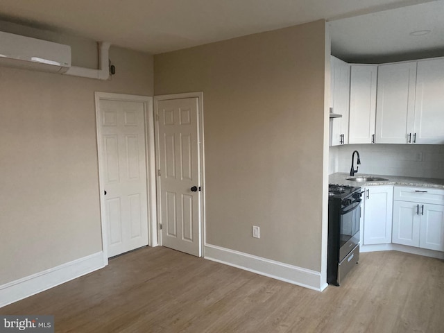 kitchen featuring a wall mounted air conditioner, light wood-type flooring, gas stove, sink, and white cabinetry