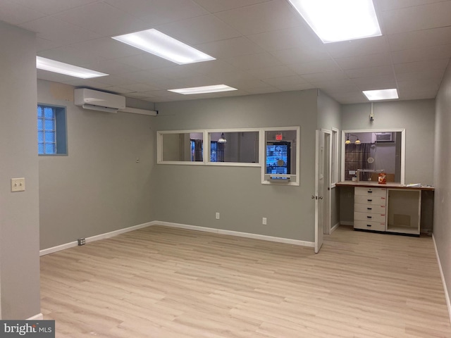 basement with a wall mounted air conditioner, a drop ceiling, and light wood-type flooring