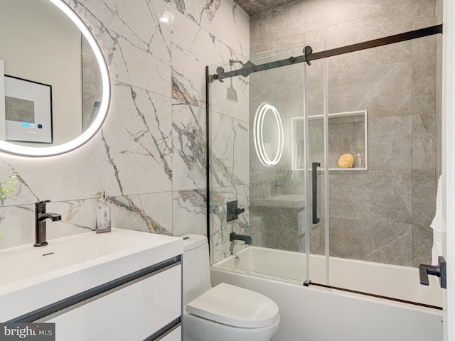 full bathroom with combined bath / shower with glass door, vanity, toilet, and tile walls