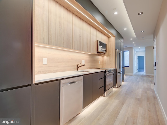 kitchen featuring light brown cabinets, sink, light wood-type flooring, appliances with stainless steel finishes, and tasteful backsplash