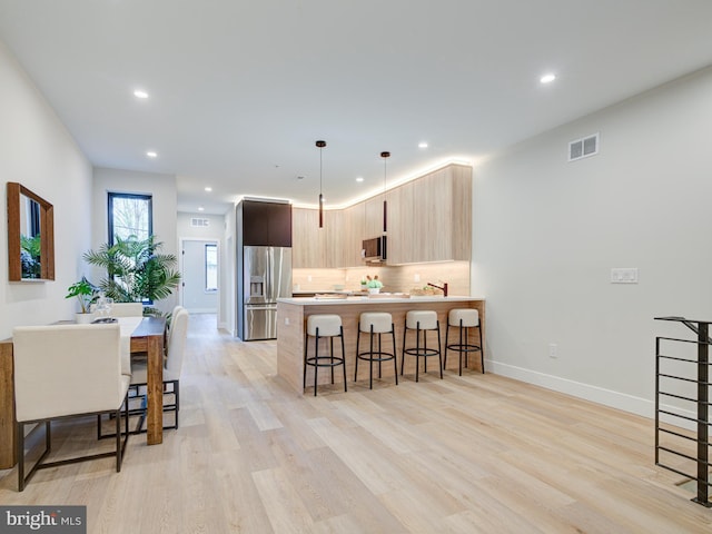 kitchen with a kitchen breakfast bar, light hardwood / wood-style flooring, decorative light fixtures, light brown cabinetry, and appliances with stainless steel finishes