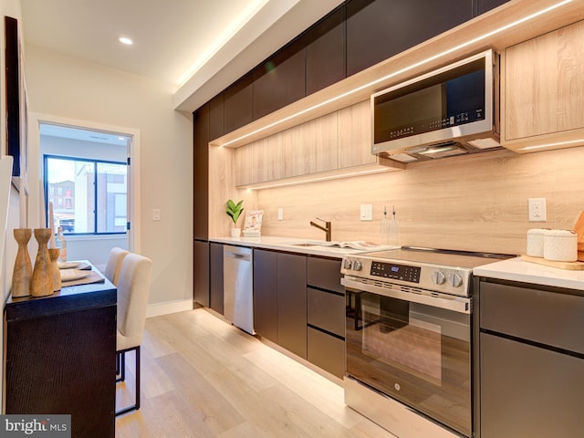 kitchen with tasteful backsplash, light brown cabinetry, light hardwood / wood-style flooring, and appliances with stainless steel finishes