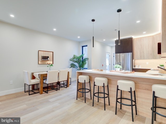 kitchen featuring hanging light fixtures, stainless steel refrigerator with ice dispenser, light hardwood / wood-style floors, light brown cabinetry, and a breakfast bar