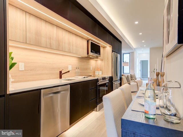 kitchen with backsplash, stainless steel appliances, sink, light brown cabinets, and light hardwood / wood-style floors