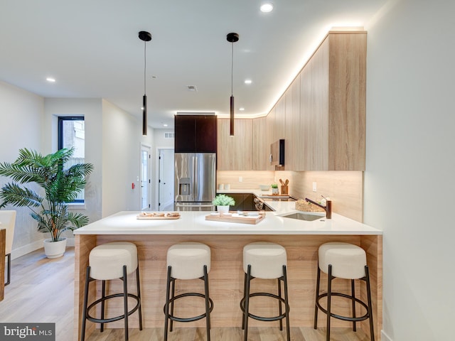 kitchen with pendant lighting, light brown cabinets, sink, light wood-type flooring, and stainless steel fridge with ice dispenser