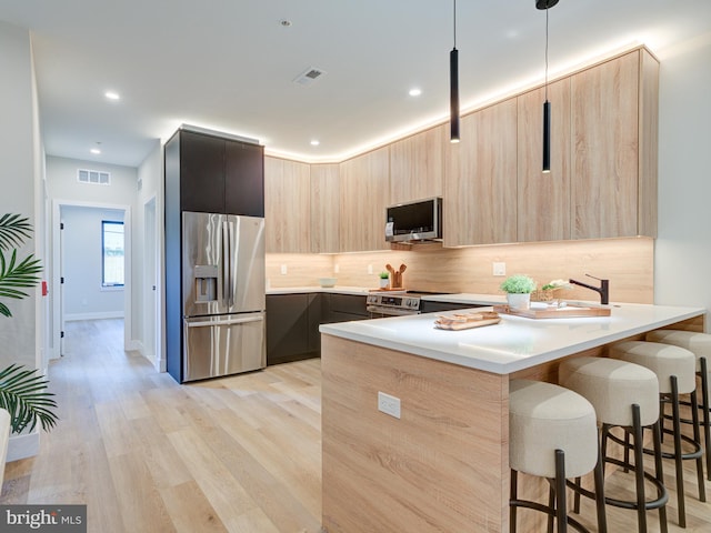 kitchen with hanging light fixtures, light hardwood / wood-style flooring, light brown cabinetry, a kitchen bar, and stainless steel appliances