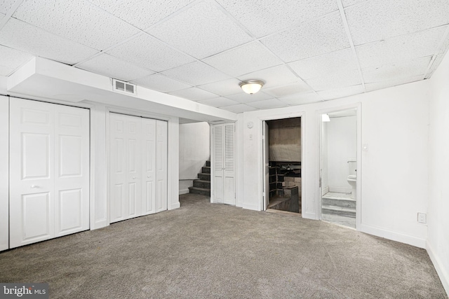 unfurnished bedroom featuring a drop ceiling, multiple closets, connected bathroom, and carpet floors