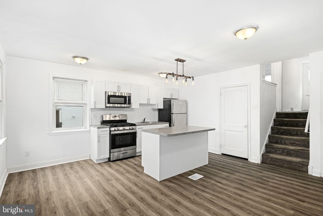 kitchen with pendant lighting, white cabinets, appliances with stainless steel finishes, a center island, and dark hardwood / wood-style floors