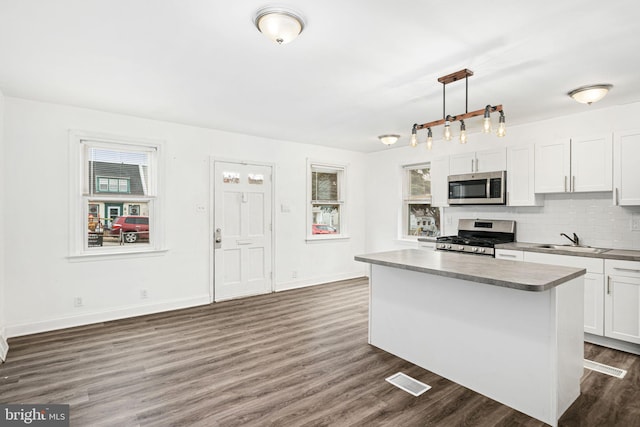 kitchen featuring a kitchen island, decorative light fixtures, white cabinetry, stainless steel appliances, and sink