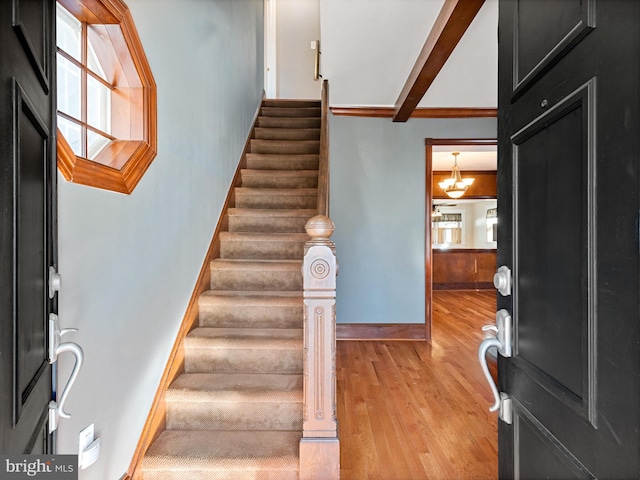 entryway featuring beamed ceiling, light hardwood / wood-style floors, and an inviting chandelier