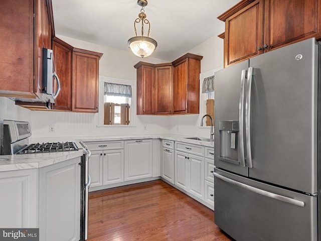 kitchen featuring hanging light fixtures, sink, appliances with stainless steel finishes, white cabinetry, and wood-type flooring