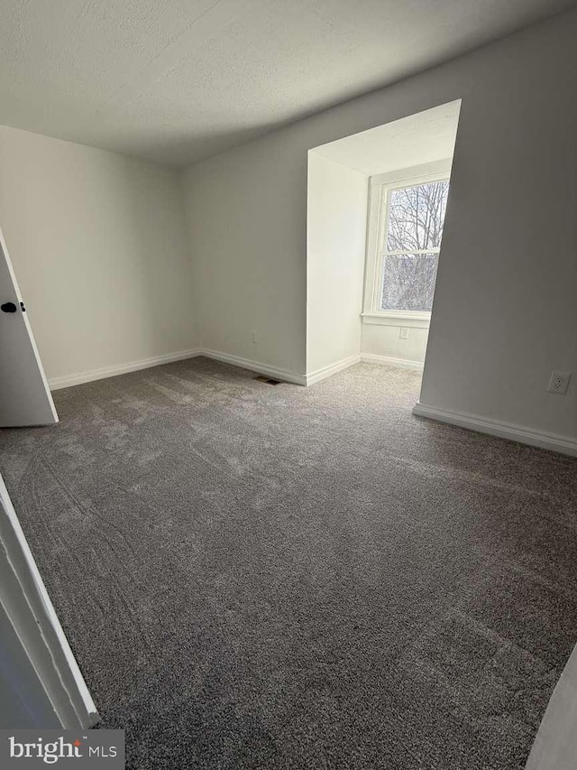 spare room with dark colored carpet and a textured ceiling