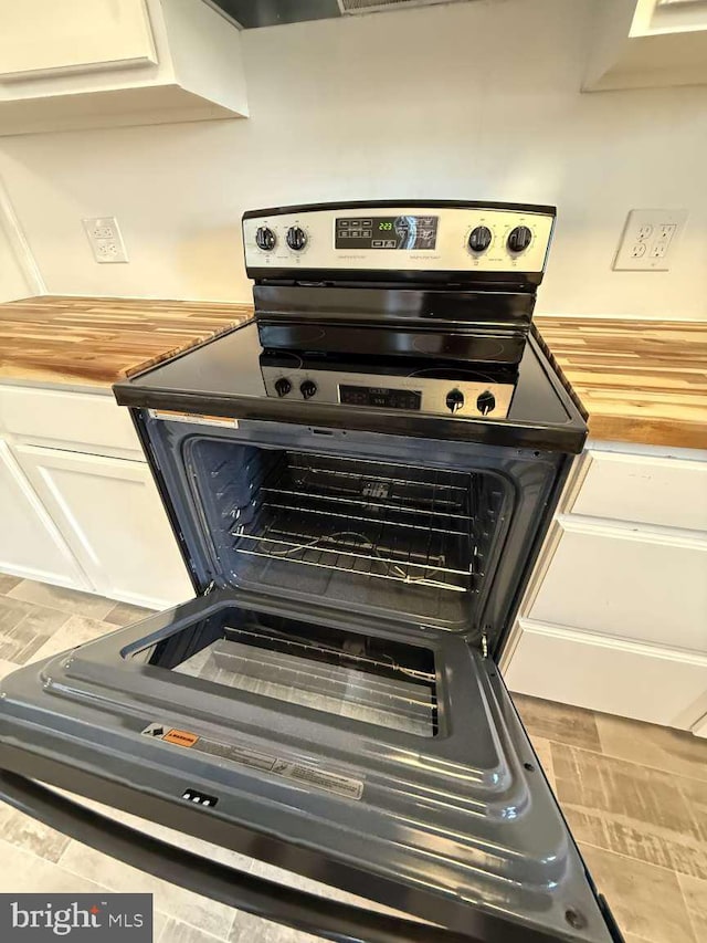 interior details featuring butcher block countertops, electric range, and white cabinetry