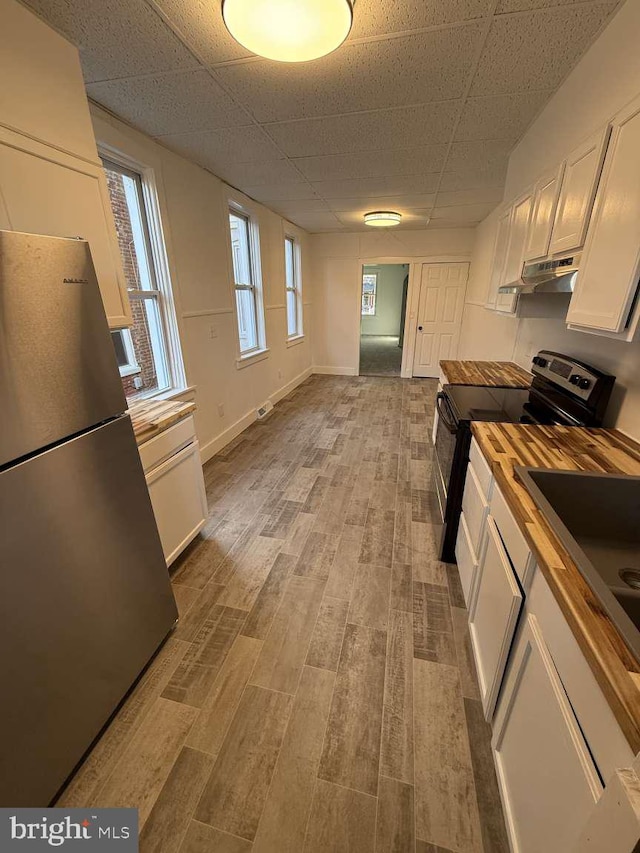 kitchen featuring black electric range oven, wooden counters, stainless steel fridge, white cabinets, and light wood-type flooring