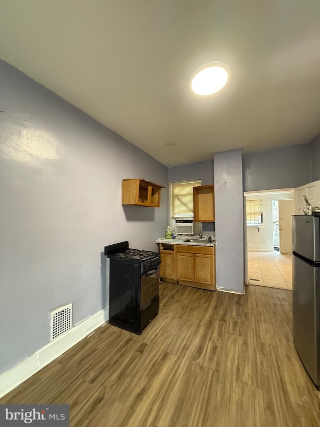 kitchen with stainless steel fridge, sink, light hardwood / wood-style flooring, and black stove