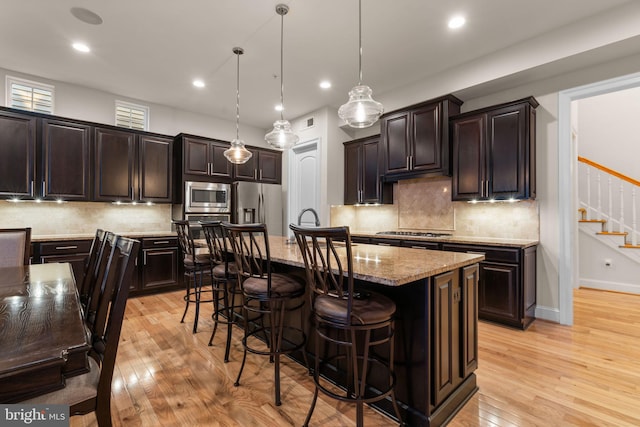 kitchen featuring a breakfast bar, stainless steel appliances, a kitchen island with sink, light hardwood / wood-style flooring, and hanging light fixtures