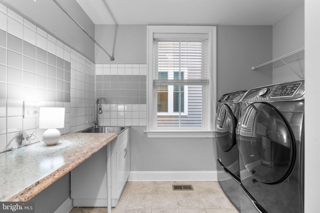 clothes washing area with washer and dryer, light tile patterned floors, sink, and tile walls