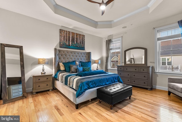 bedroom featuring multiple windows, light wood-type flooring, a tray ceiling, and ceiling fan