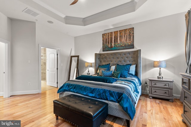 bedroom featuring ceiling fan, ensuite bathroom, light hardwood / wood-style floors, a tray ceiling, and ornamental molding