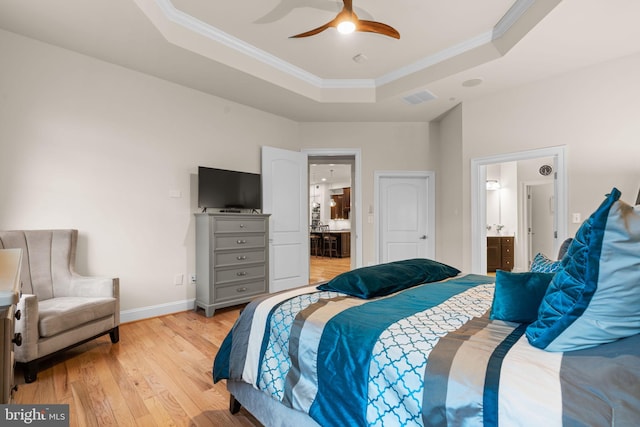 bedroom featuring connected bathroom, ceiling fan, crown molding, light hardwood / wood-style floors, and a tray ceiling