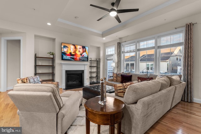 living room with ceiling fan, light wood-type flooring, crown molding, and a tray ceiling