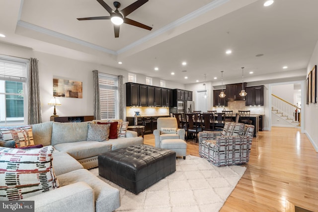 living room featuring light wood-type flooring, a tray ceiling, and crown molding