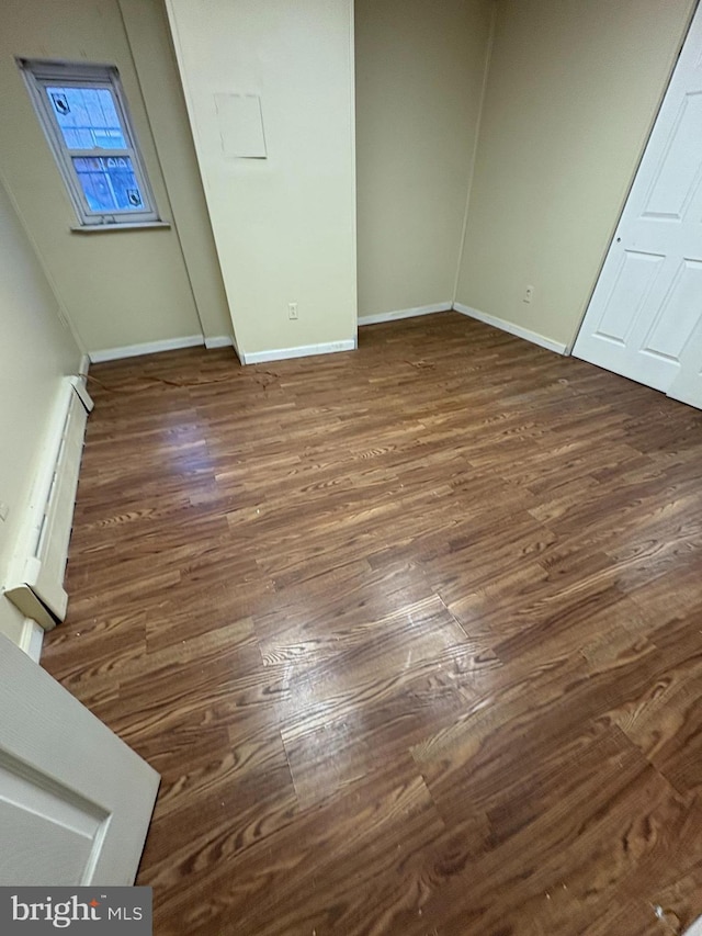 unfurnished bedroom featuring baseboards, baseboard heating, and dark wood-type flooring