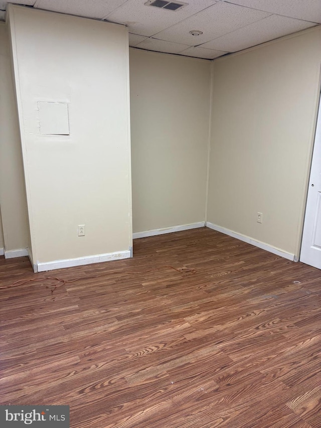 unfurnished room with a paneled ceiling, dark wood-style flooring, visible vents, and baseboards