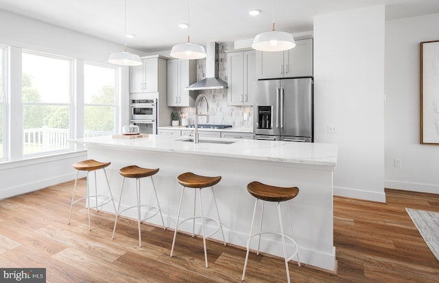 kitchen with a kitchen bar, light wood-type flooring, stainless steel appliances, wall chimney range hood, and gray cabinets