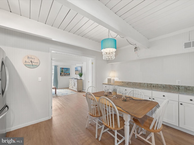 dining area with a notable chandelier, visible vents, light wood-type flooring, beamed ceiling, and baseboards