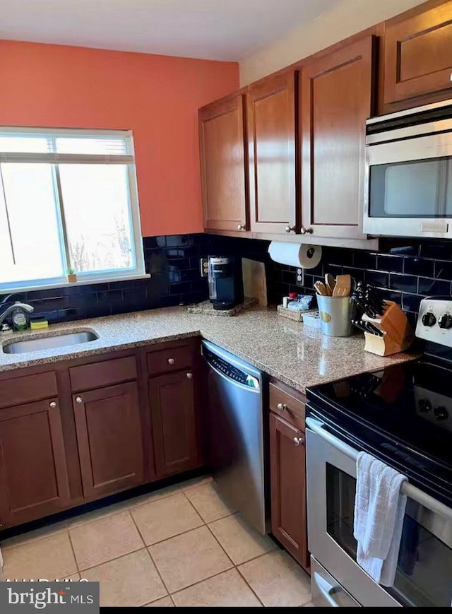 kitchen featuring sink, light stone counters, decorative backsplash, light tile patterned floors, and appliances with stainless steel finishes