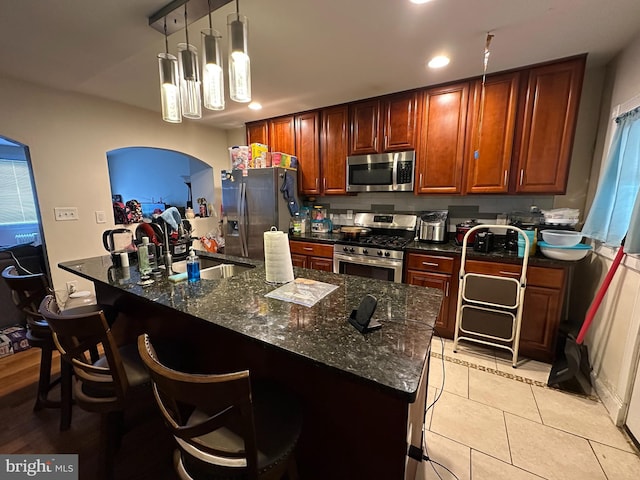 kitchen featuring appliances with stainless steel finishes, decorative light fixtures, a breakfast bar area, dark stone countertops, and light tile patterned floors