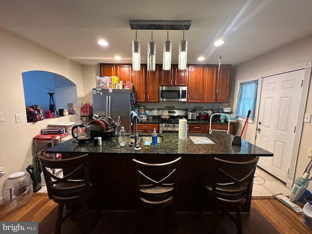 kitchen with a kitchen island with sink, sink, pendant lighting, and appliances with stainless steel finishes