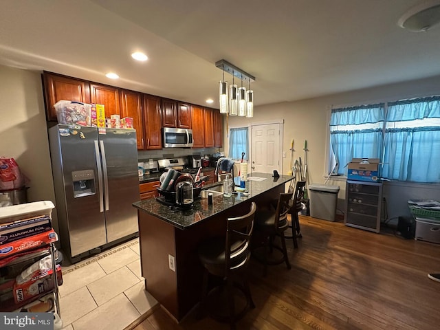 kitchen with a breakfast bar, sink, dark stone counters, hanging light fixtures, and stainless steel appliances