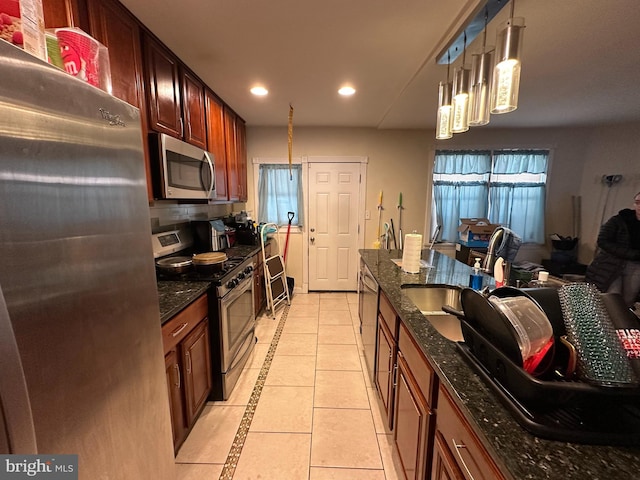 kitchen featuring sink, hanging light fixtures, dark stone countertops, light tile patterned floors, and appliances with stainless steel finishes