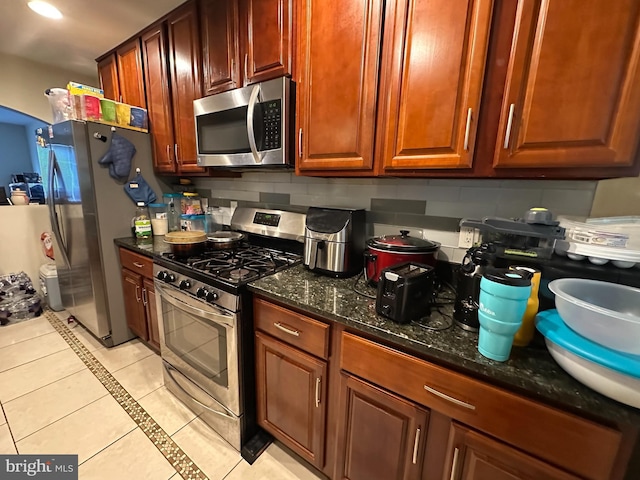 kitchen with stainless steel appliances, dark stone countertops, backsplash, and light tile patterned floors