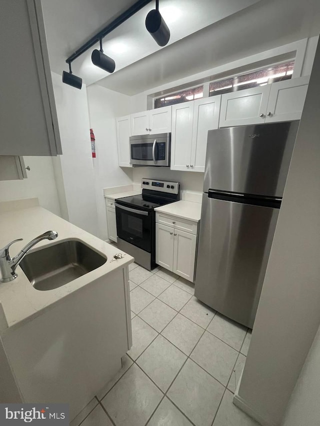 kitchen with white cabinets, stainless steel appliances, light tile patterned flooring, and sink