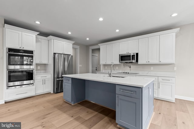 kitchen featuring sink, white cabinetry, light hardwood / wood-style flooring, appliances with stainless steel finishes, and an island with sink