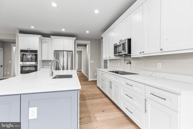 kitchen featuring appliances with stainless steel finishes, white cabinetry, sink, a kitchen island with sink, and light stone counters