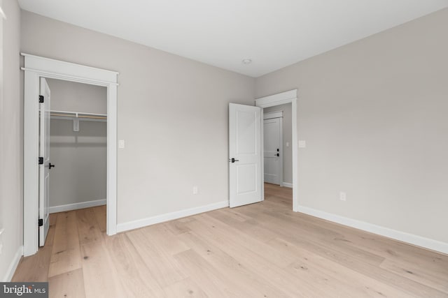 unfurnished bedroom with a walk in closet, a closet, and light wood-type flooring