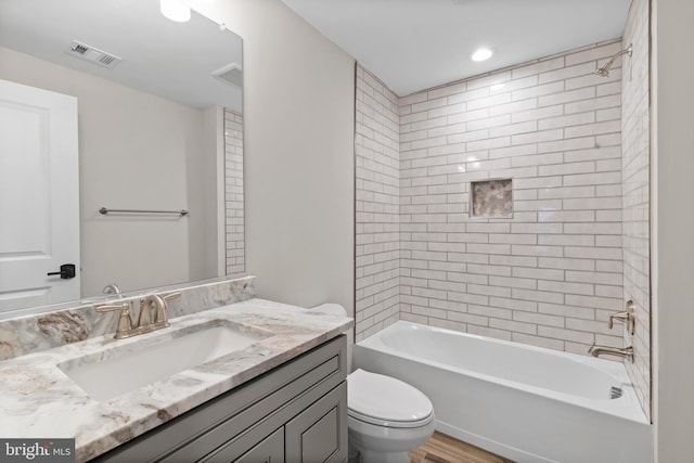 full bathroom featuring vanity, tiled shower / bath, and toilet