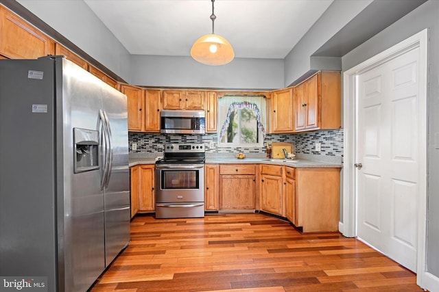 kitchen featuring stainless steel appliances, tasteful backsplash, sink, hanging light fixtures, and light hardwood / wood-style flooring