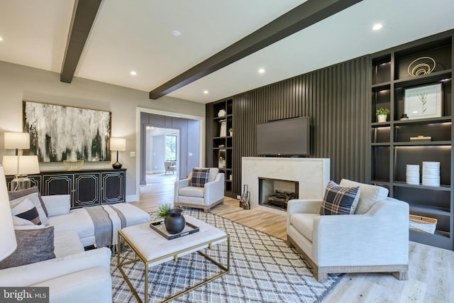 living room with beam ceiling, built in shelves, light hardwood / wood-style flooring, and a high end fireplace