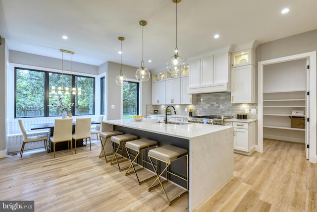 kitchen featuring decorative backsplash, sink, pendant lighting, white cabinets, and an island with sink