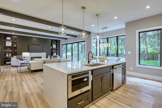 kitchen with pendant lighting, a center island with sink, sink, light wood-type flooring, and beam ceiling