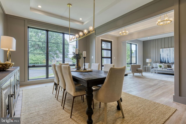 dining area with a tray ceiling, a notable chandelier, and light wood-type flooring