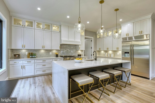 kitchen featuring a center island with sink, white cabinetry, built in fridge, and sink