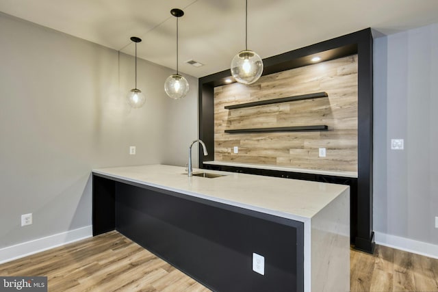 bar with sink, hanging light fixtures, light stone counters, wood walls, and light wood-type flooring